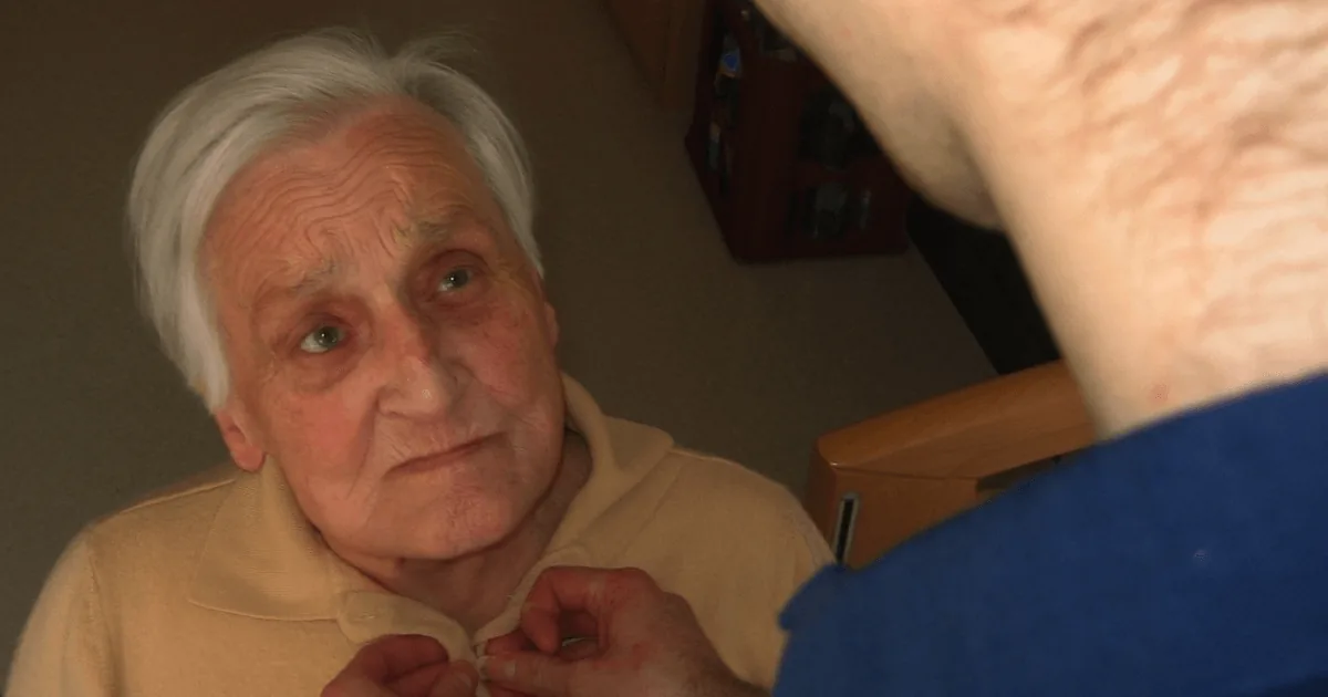 Idosa sendo auxiliada a se vestir, ilustrando cuidados relacionados à doença de Alzheimer